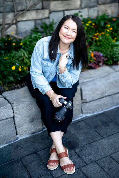 Ann, Orlando senior photographer and mom of five, smiling while seated with her camera at a natural light portrait location—Petal and Stone Photography.