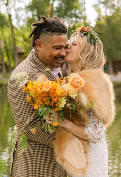 Colorado wedding photographer capturing a couple embracing outdoors with a vibrant fall bouquet