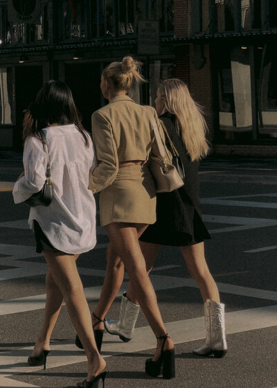 Three girls walking arm in arm down sidewalk together