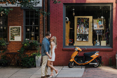 A groom and bride hold hands facing one another in Lancaster City. they are on Gallery Row, and there is an orange vespa in the 