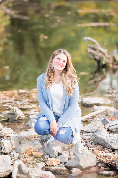 High school senior girl leans against a wooden backdrop outside in white dress for senior portraits