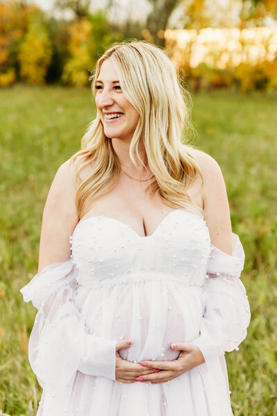 Beautiful mama to be holding her baby bump as she smiles while looking over her shoulder captured by  Green Bay Family photographer Ashley Kalbus