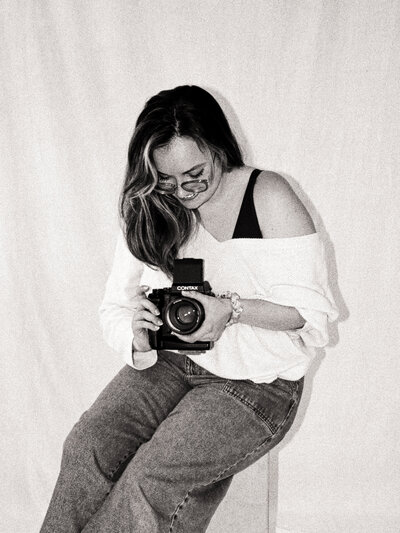 Black and white film portrait of Dominique, seated and looking down while holding a Contax camera — co-founder and film wedding photographer at Castillo Holliday Photo + Film.