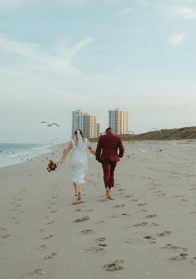 fun bride and groom run towards seagulls on beach