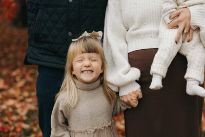 Blonde little girl smiling at camera while holding mother's hand