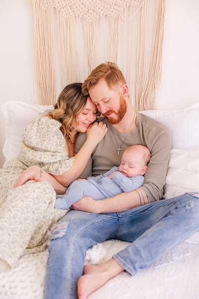 Family of 3 snuggling together during their lifestyle newborn session at a photo studio in Fredrick, Colorado. 