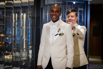 Groom tapping groom on the shoulder both dressed in white tuxes with white boutineers
