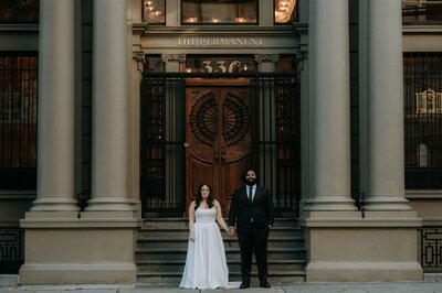 Couple holding hands in front of a historic building.