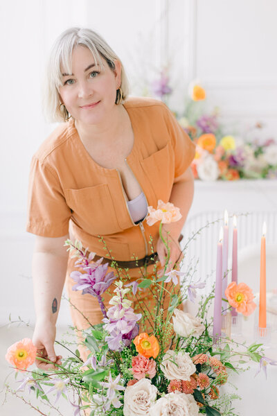 A smiling woman adjusts a colourful flower arrangement at her Montreal floral studio. 
