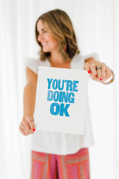 woman holding a sign that reads you're doing ok