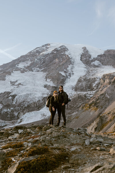 A couple stands on top of a mountain in front of Mt. Rainier  in Washington.