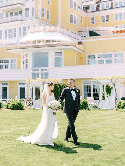 Bride and groom smiling and walking across the lawn with Ocean House Rhode Island in the background