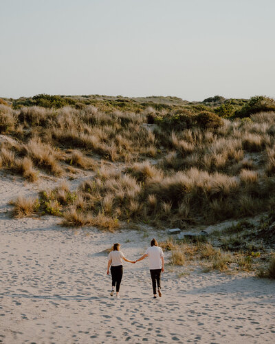 twee vrouwen lopen hand in hand door de duinen