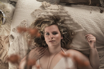 Photo femme allongée sur le dos sur un lit, dans un décor bohème, séance photo bienveillante
