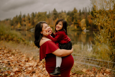 Pregnant mom and daughter laughing together. Mom is holding her and they are both wearing red.
