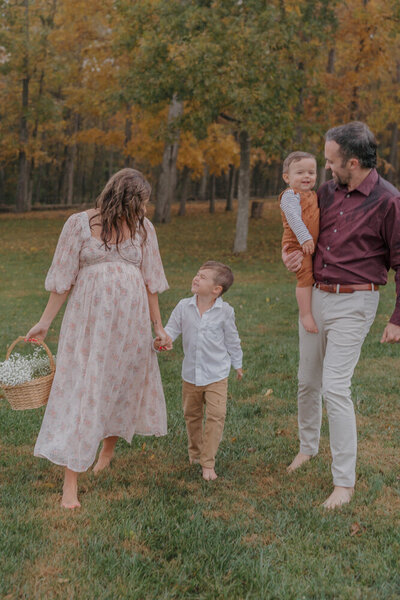 A mother holds the hand of her young son in one hand and a basket of Baby's Breath in the other. The father is next to them holding their younger son, looking at him and smiling.