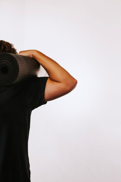 Alex Paige in a red tank and black shorts doing a yoga pose against a wall