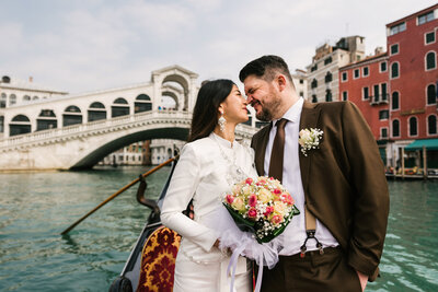 The bride and groom arrive at their wedding in a gondola, with the iconic Rialto Bridge providing a picturesque backdrop to this enchanting Venetian celebration