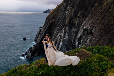 married couple looking over cliff , bride is in a long flowing dress, photo by Portland elopement photographer 