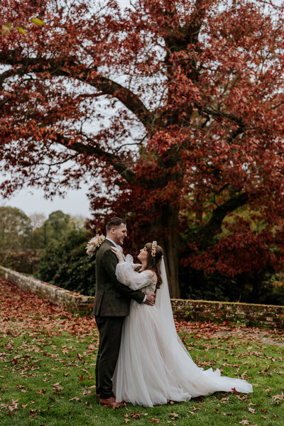 A bride and groom sit on a pub bench and embrace outside King's Chapel Amersham