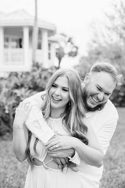 Black and white photo of couple hugging and laughing, just engaged