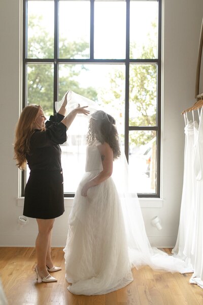 Bride trying on a wedding dress as a stylist adjusts her veil.