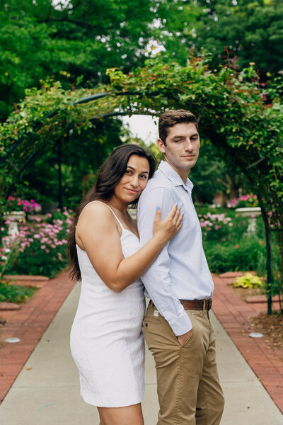 Woman gently leaning on her fiancé’s back while he looks over his shoulder at her with a soft smile.