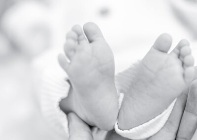 Sweet black and white newborn portrait, natural baby photography, Birmingham newborn photographer – A precious newborn baby lying on a soft blanket, dressed in a delicate white onesie. Their gentle expression and tiny hands create a timeless and heartfelt moment.