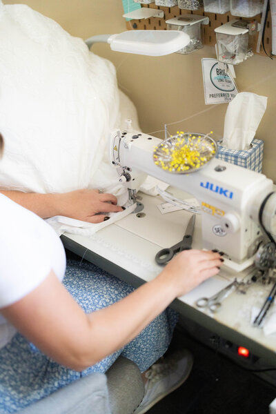 Close-up of hands working on a sewing machine, altering a wedding dress.