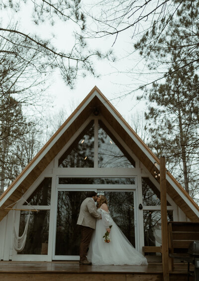couple kissing in front of a modern A-frame cabin during an intimate forest elopement