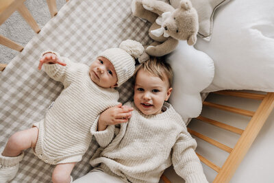 Toddler and newborn baby lie in cot looking at camera during  home photography 