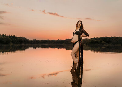 Photo of a pregnant woman standing in lake. She is wearing black underwear