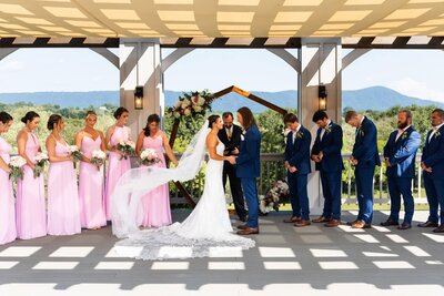 Newlyweds share an epic first kiss as their wedding party cheers under tented outdoor ceremony space with a small pond in the background
