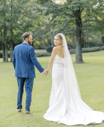 Groom in blue suit and bride in white gown holding hands in a field