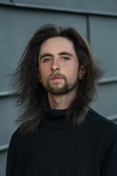 A person with long hair and a beard with a serious look on their face