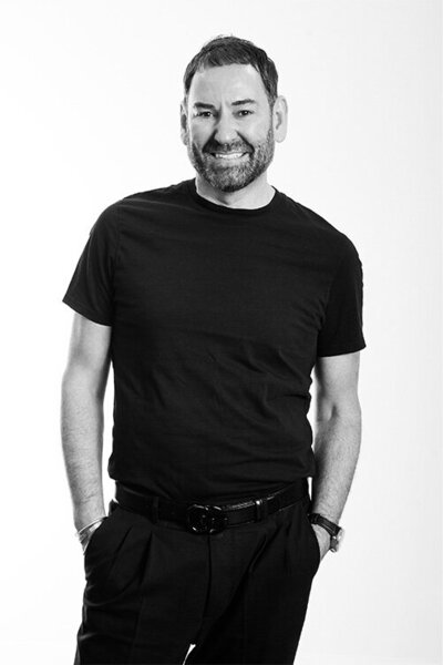 Confident male Salon Owner & Director wearing a black t-shirt, showcasing leadership and expertise in professional hairdressing services.