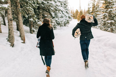 candid photo of couple walking in snow carrying wood for fire