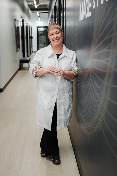 Kirsty Shelley leaning on a salon wall in her lab coat