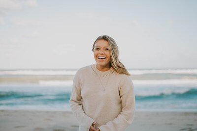 Serena Girardi, sleep consultant, smiles on the beach in a tan sweater