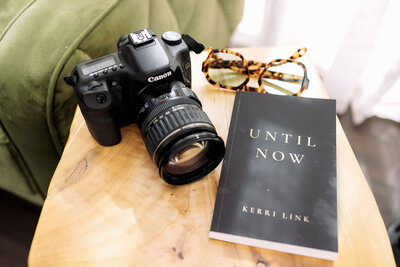 Close-up of Kerri Link’s book Until Now beside a camera and pen, symbolizing creativity, healing, and storytelling.