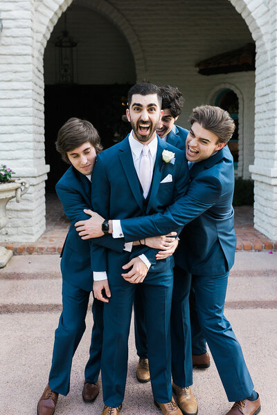 Groom with groomsmen hugging him from behind