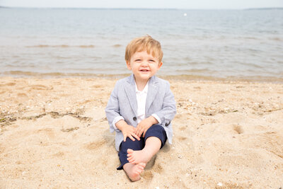 Little boy sits on log in yellow flowers with stuffed animal smiling at camera