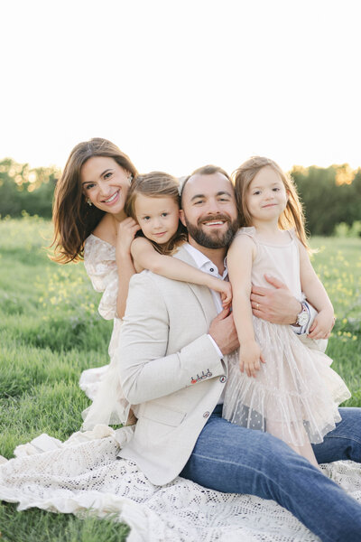 family of 4 sitting on a field at arbor hills nature preserve smiling at the camera at sunset
