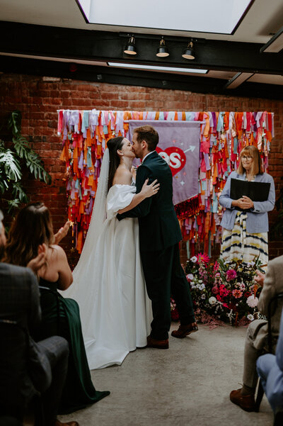 A couple stand in front of a custom wedding banner and backdrop at their wedding at The Shack Revolution.
