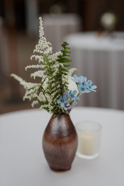 Small bud vase with greenery and blue flowers on table