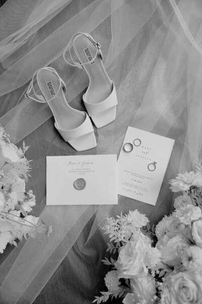 Flat lay featuring a bride’s veil, modern square-toe bridal shoes, and white florals alongside a wedding invitation with a gold wax seal and wedding rings, ideal for wedding stationery inspiration in Ottawa.