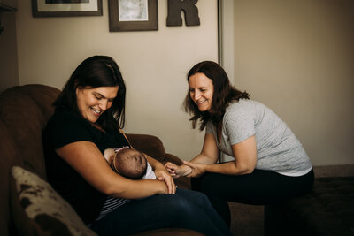 Midwife smiling during home visit as mother breastfeeds her baby