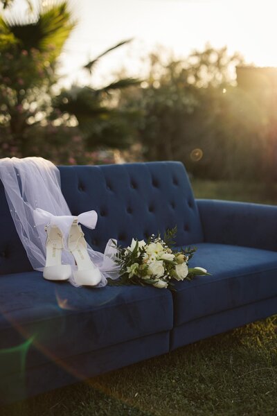 Flowers, bride's shoes, and veil sitting on velvet blue couch