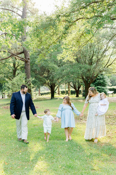 family of 4 walking holding hands in a park