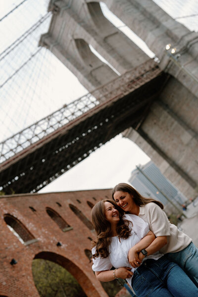 LGBTQ+ couple embracing beneath the Brooklyn Bridge during their engagement photoshoot in New York City